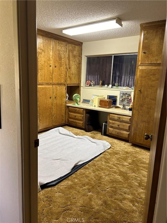 office featuring a textured ceiling, built in desk, and carpet