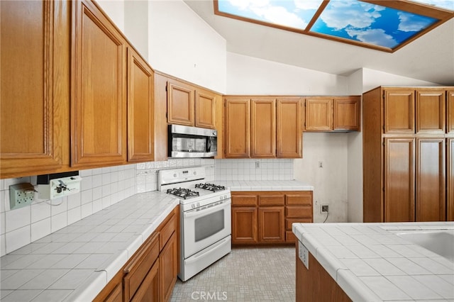 kitchen featuring decorative backsplash, white gas range oven, stainless steel microwave, lofted ceiling, and tile counters