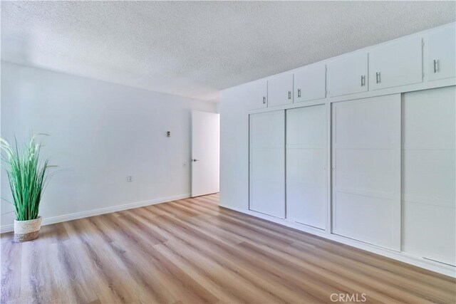 125 Via Estrada Unit B, Laguna Woods, CA 92637 - unfurnished bedroom featuring a textured ceiling, baseboards, and light wood finished floors