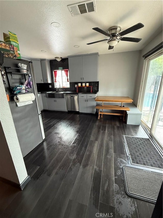 kitchen featuring visible vents, dark countertops, appliances with stainless steel finishes, a sink, and dark wood-type flooring