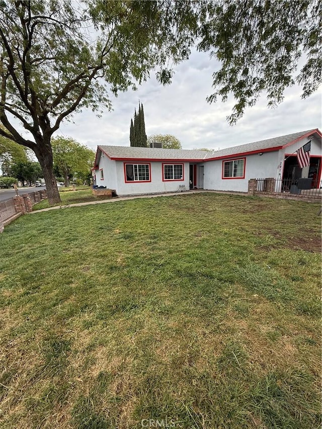 ranch-style house with fence, stucco siding, and a front lawn
