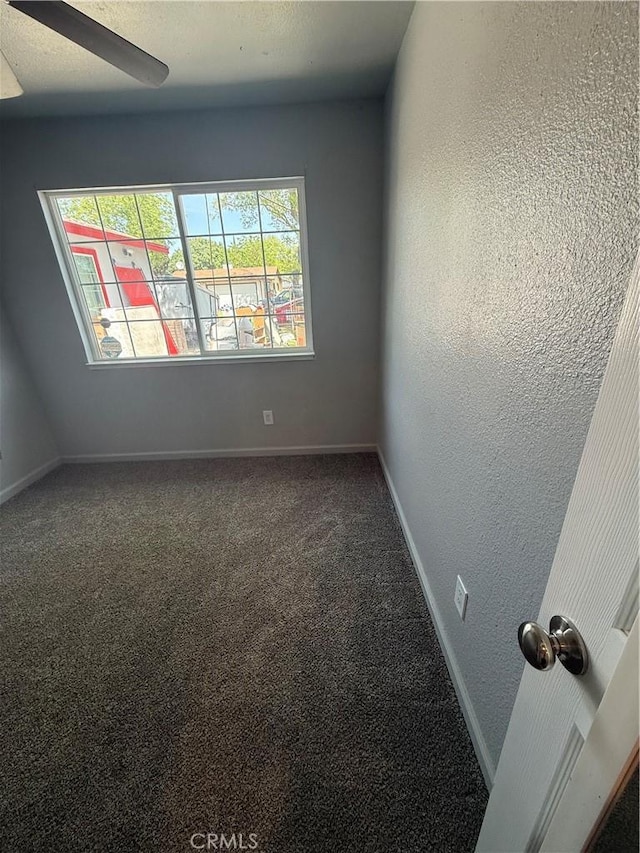 carpeted empty room with baseboards, a ceiling fan, and a textured wall