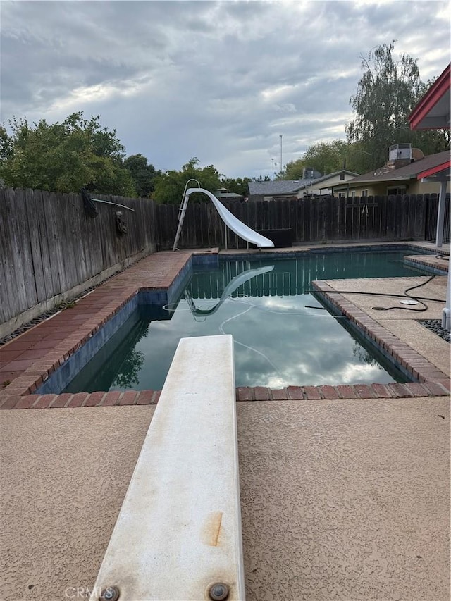view of pool with a diving board, a water slide, a fenced backyard, a fenced in pool, and a patio area