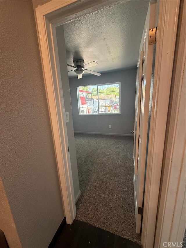 hall with dark carpet, a textured ceiling, and baseboards
