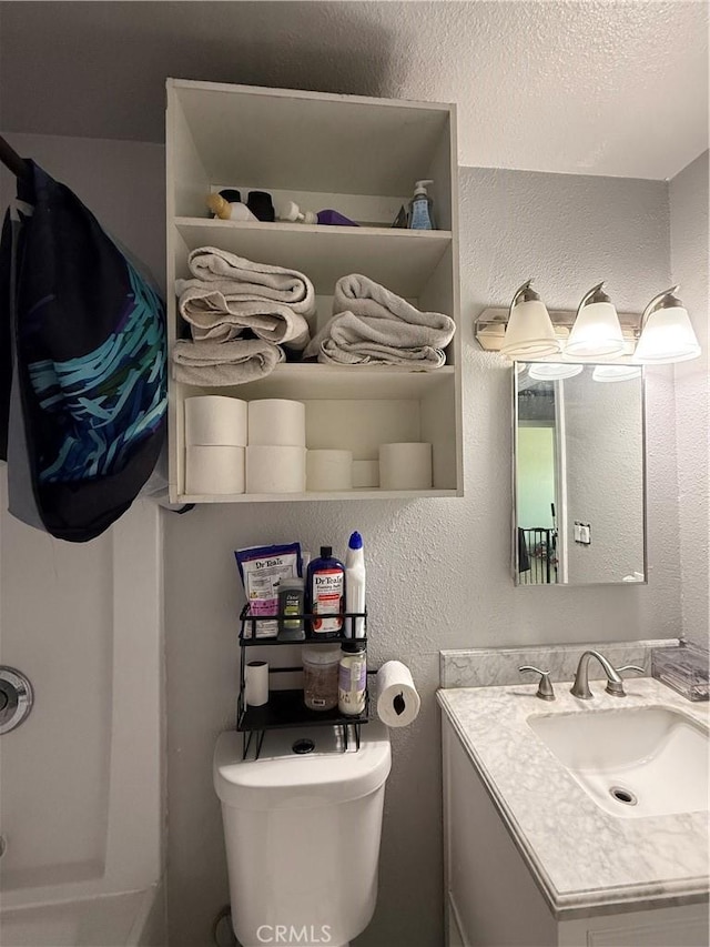 bathroom featuring toilet, a textured wall, and vanity