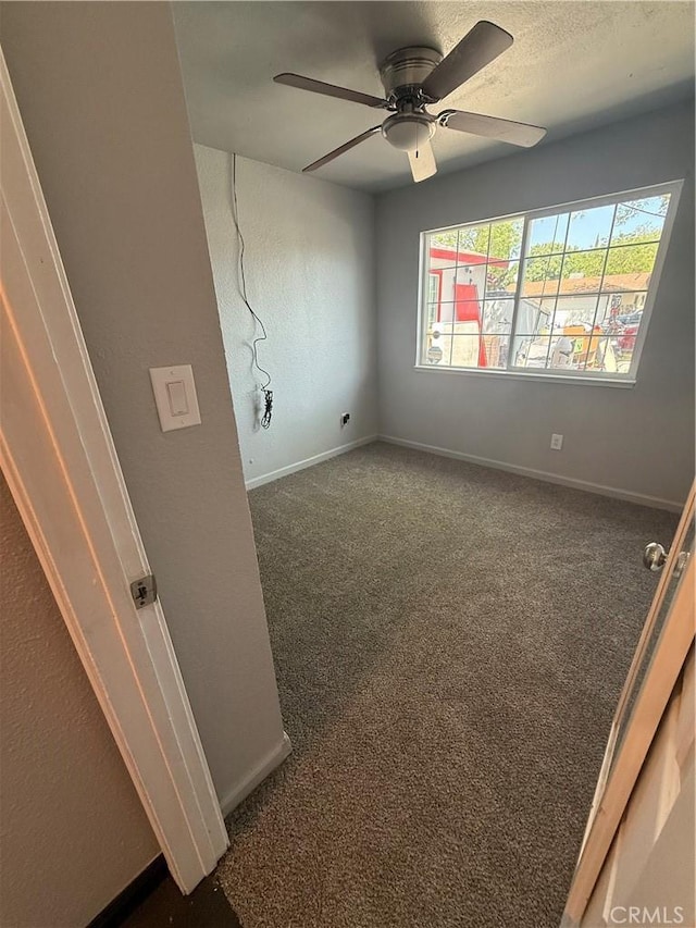 unfurnished room featuring baseboards, a ceiling fan, and dark carpet