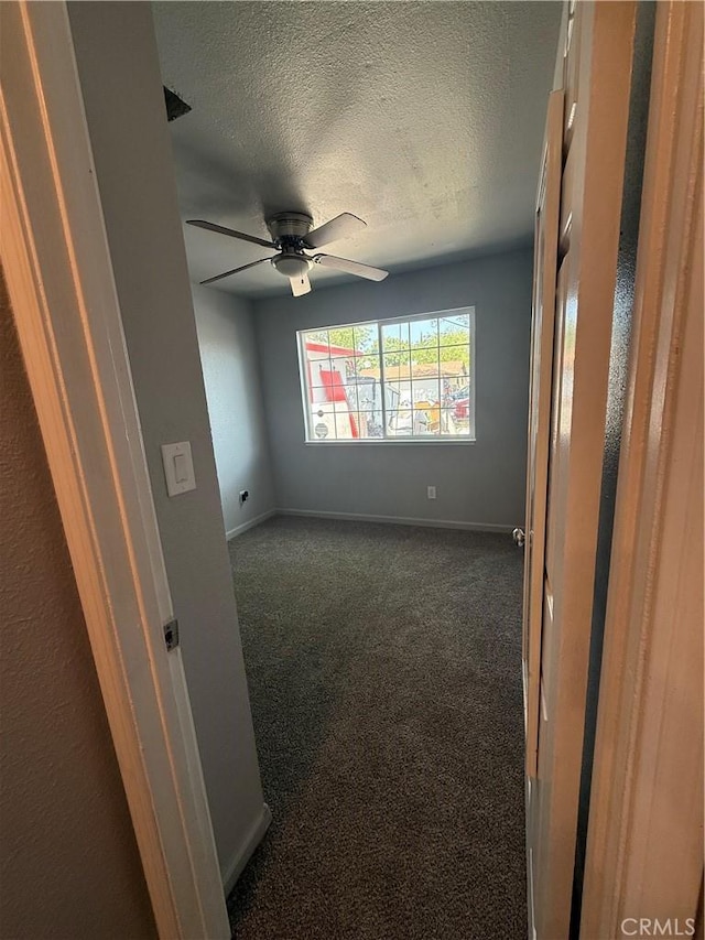 spare room featuring dark colored carpet, a textured ceiling, ceiling fan, and baseboards
