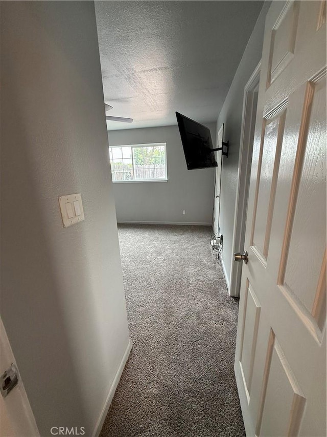 hallway with baseboards, carpet flooring, and a textured ceiling