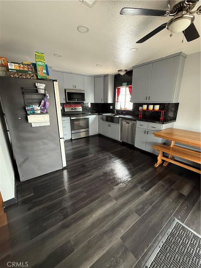 kitchen with a ceiling fan, backsplash, dark countertops, stainless steel appliances, and dark wood-type flooring