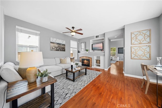 living room with visible vents, wood finished floors, a fireplace, baseboards, and a ceiling fan