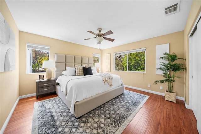 bedroom featuring baseboards, a ceiling fan, wood finished floors, and visible vents