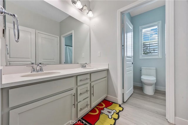 bathroom with double vanity, wood finished floors, a sink, baseboards, and toilet