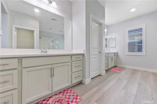 bathroom featuring a sink, baseboards, wood finished floors, and two vanities