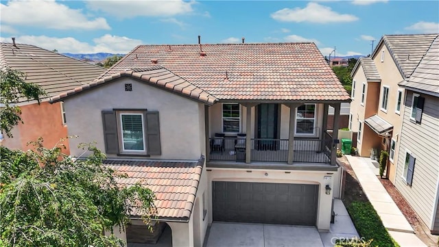 back of house with an attached garage, driveway, a tile roof, and stucco siding