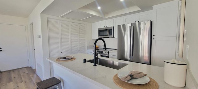 742 Eastshore Unit 98, Chula Vista, CA 91913 - kitchen featuring stainless steel appliances, white cabinets, light wood finished floors, a raised ceiling, and light stone countertops