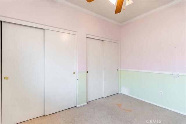 unfurnished bedroom featuring crown molding, baseboards, two closets, and carpet flooring
