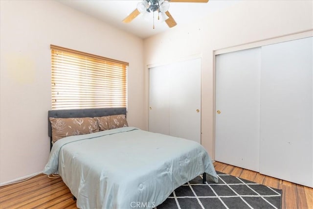 bedroom featuring two closets, ceiling fan, and wood finished floors