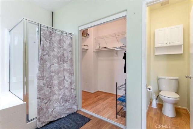 full bathroom featuring toilet, a walk in closet, a shower stall, and wood finished floors