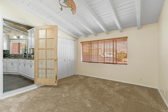 unfurnished bedroom featuring baseboards, vaulted ceiling with beams, and dark colored carpet