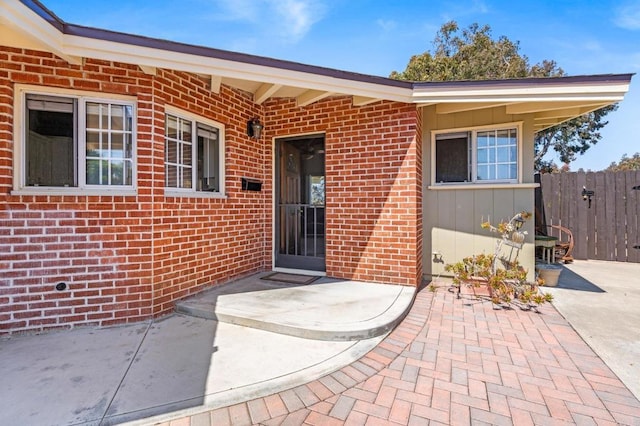 property entrance with fence, a patio, and brick siding