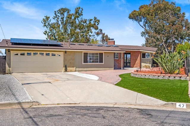 ranch-style house with a front lawn, a garage, a chimney, solar panels, and driveway