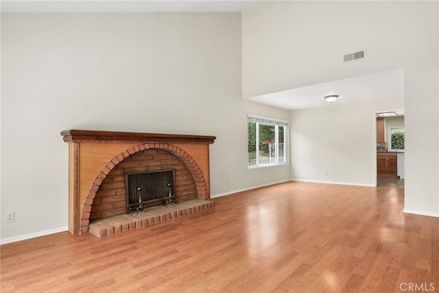unfurnished living room with visible vents, wood finished floors, a fireplace, baseboards, and a high ceiling