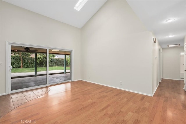 unfurnished room with light wood-style floors, high vaulted ceiling, and baseboards