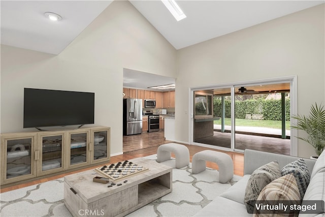 living area featuring baseboards, a ceiling fan, wood finished floors, and high vaulted ceiling