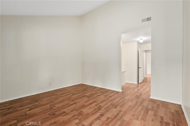 unfurnished room featuring baseboards, visible vents, wood finished floors, and a towering ceiling