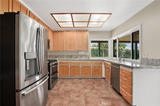 kitchen with stainless steel appliances, light stone countertops, a sink, and light brown cabinets