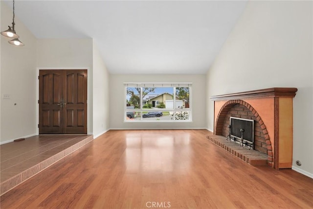 unfurnished living room featuring high vaulted ceiling, baseboards, a brick fireplace, and wood finished floors