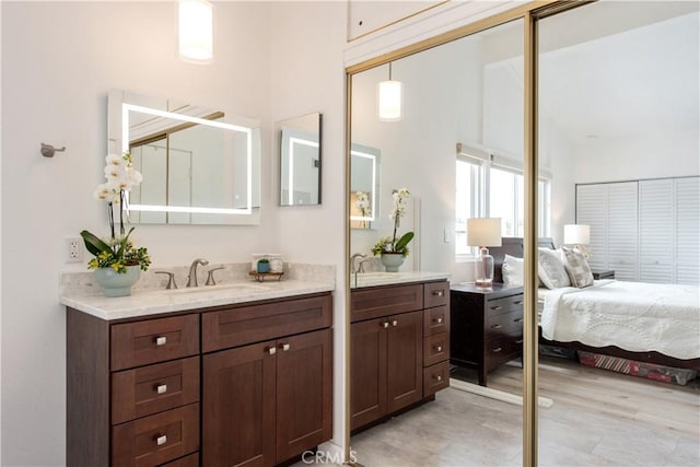 ensuite bathroom with connected bathroom, wood finished floors, two vanities, and a sink