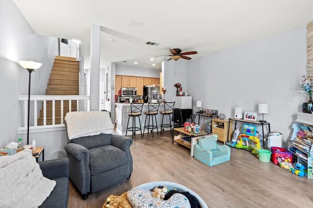 living area with visible vents, ceiling fan, wood finished floors, and stairway