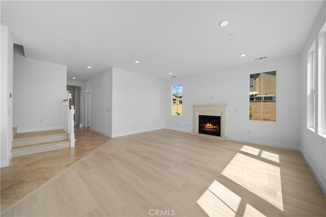 unfurnished living room featuring a lit fireplace, healthy amount of natural light, recessed lighting, and baseboards
