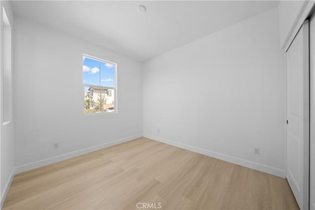 unfurnished bedroom featuring light wood-style flooring, baseboards, and a closet