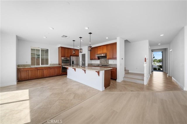 kitchen with stainless steel appliances, a sink, under cabinet range hood, recessed lighting, and a breakfast bar