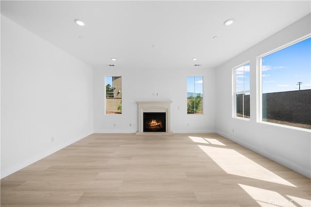 unfurnished living room featuring a lit fireplace, light wood-style flooring, recessed lighting, and baseboards