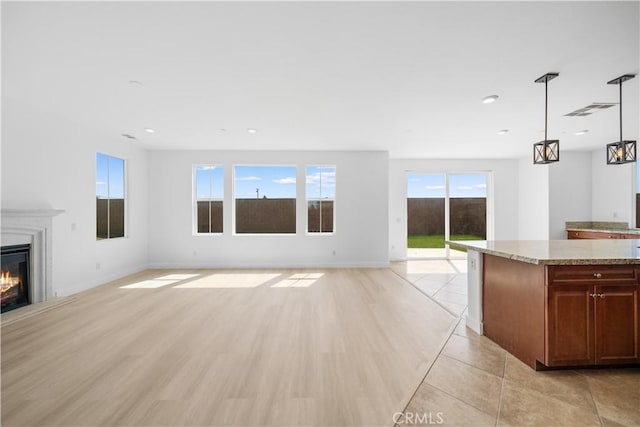 unfurnished living room with a glass covered fireplace, baseboards, recessed lighting, and light wood-type flooring