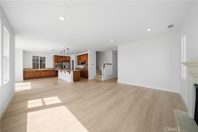 unfurnished living room featuring a sink, a high end fireplace, recessed lighting, light wood-type flooring, and baseboards