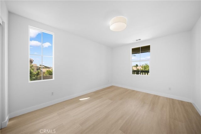 empty room with healthy amount of natural light, light wood-type flooring, and baseboards
