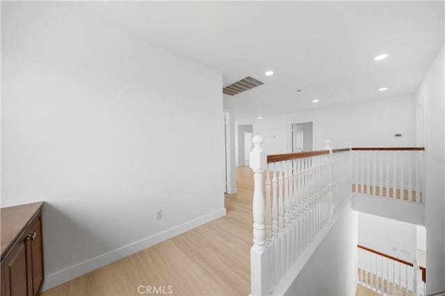 hallway with an upstairs landing, light wood-style floors, baseboards, and recessed lighting