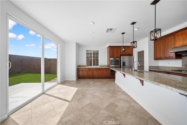 kitchen featuring a sink, appliances with stainless steel finishes, light stone counters, a breakfast bar area, and decorative light fixtures