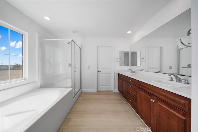 full bath featuring a stall shower, wood finished floors, double vanity, a bath, and recessed lighting