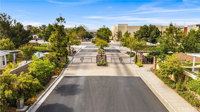 view of asphalt road with a gate, curbs, sidewalks, and a gated entry