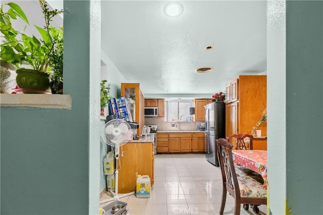 12036 Jouett St, Sylmar, CA 91342 - kitchen featuring stainless steel appliances, light countertops, light tile patterned floors, brown cabinets, and decorative backsplash