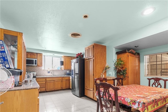 12036 Jouett St, Sylmar, CA 91342 - kitchen with stainless steel appliances, light countertops, decorative backsplash, light tile patterned flooring, and brown cabinetry