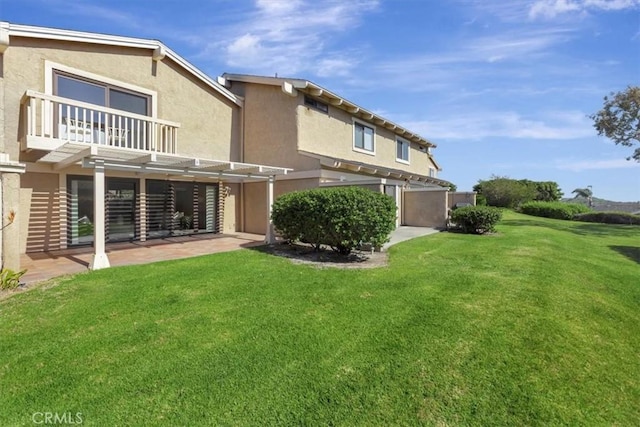 back of house featuring a lawn, a pergola, a balcony, and stucco siding
