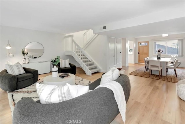 living room featuring visible vents, light wood-style flooring, and stairway