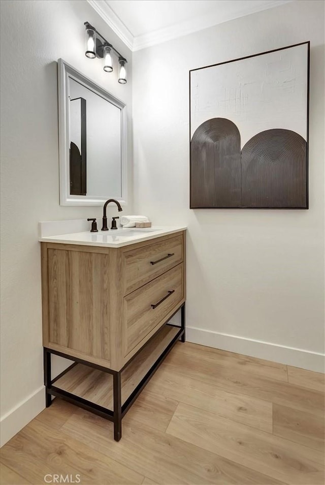 bathroom featuring baseboards, ornamental molding, wood finished floors, and vanity