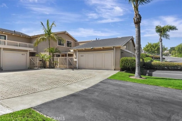 view of front facade featuring fence, stucco siding, an attached garage, and driveway